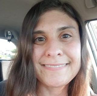 A woman with long dark hair smiling at the camera inside a car