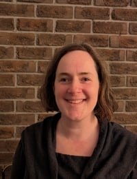 Woman with long dark hair smiling at camera against a red brick wall background